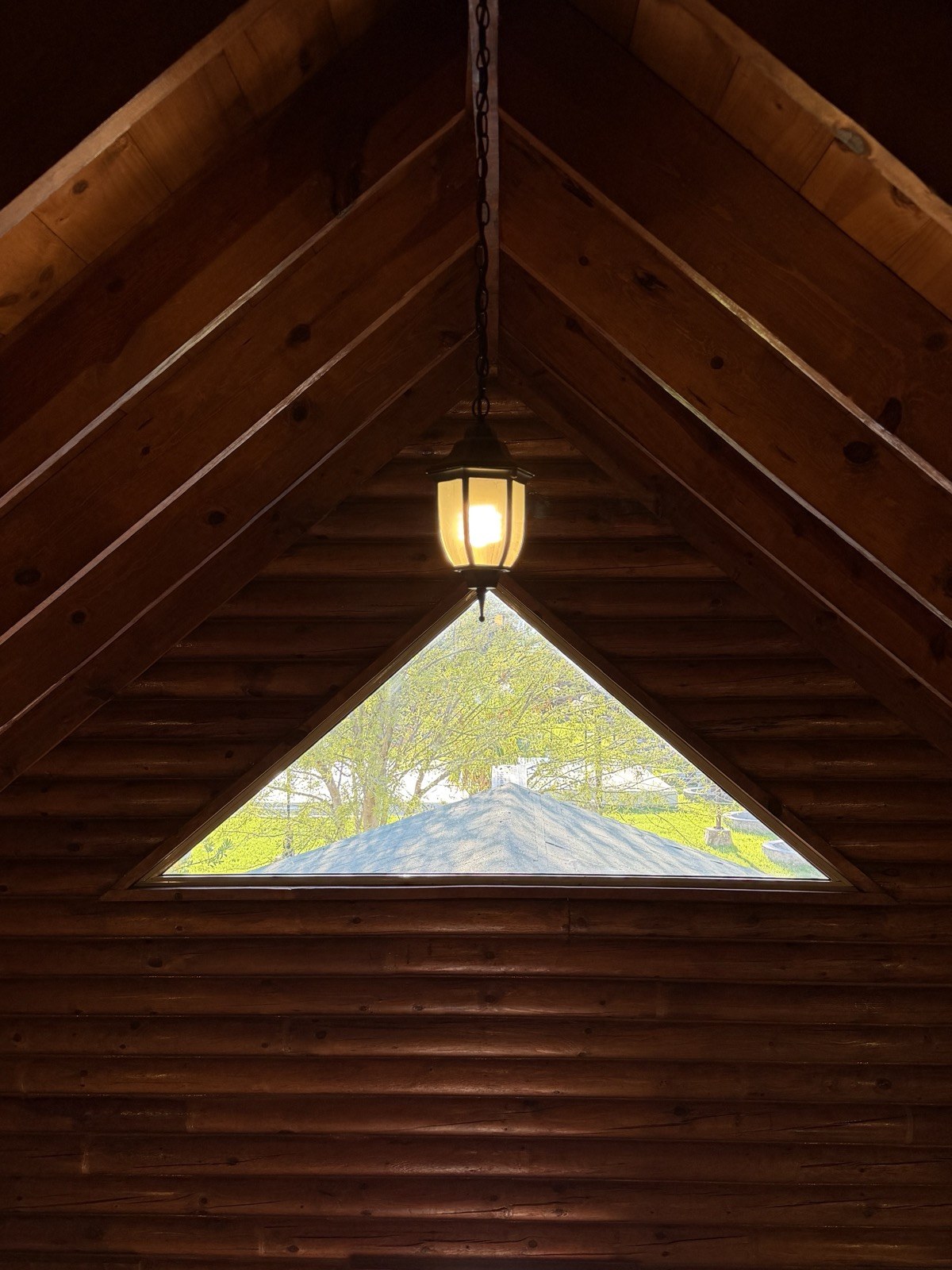 Interior de la Cabaña Grande Familiar con techo de madera y ventana triangular al jardín en Cabañas Madison, San Buenaventura, Coahuila